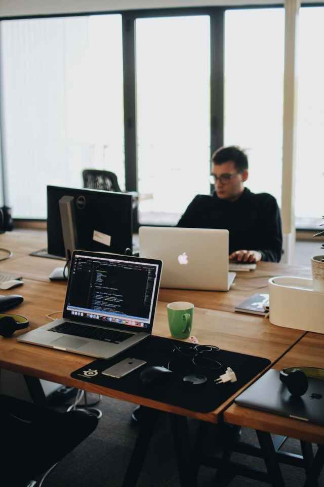 homem de camisa preta sentado atrás de uma mesa com computadores