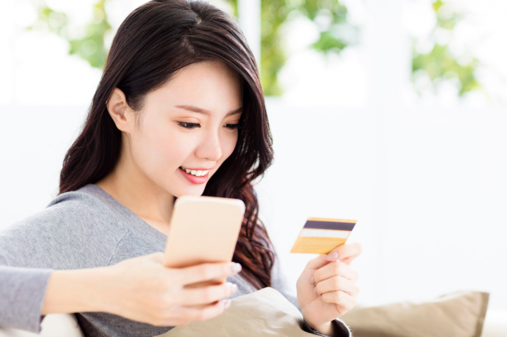 Image d'une jeune femme faisant des achats sur un site de commerce électronique à l'aide d'un téléphone portable et d'une carte de crédit. Le commerce électronique a changé le comportement des clients à la fois en ligne et hors ligne.