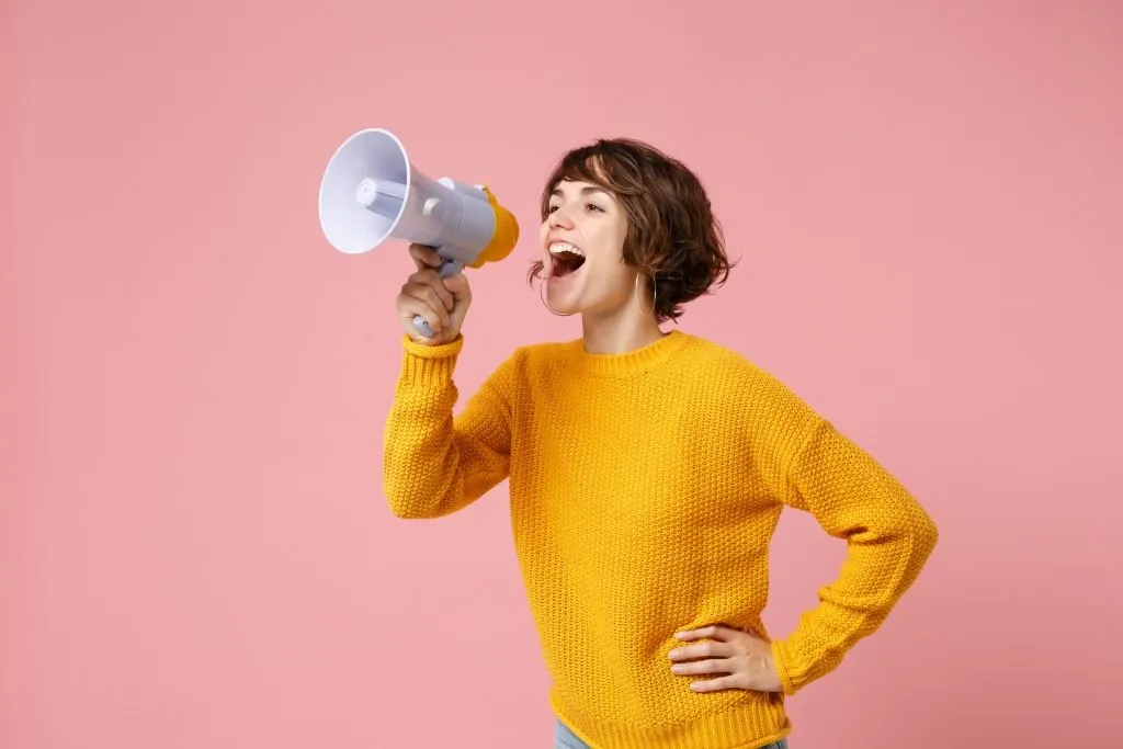 Uma jovem de suéter amarelo fala em um megafone