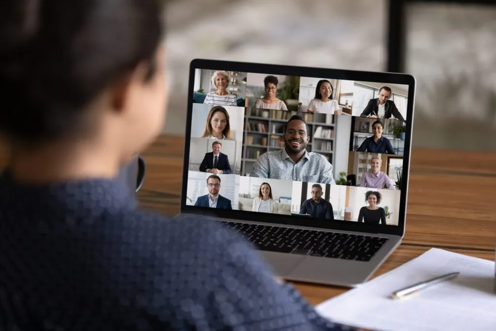 Uma mulher participando de uma reunião de videoconferência em seu laptop e interagindo com outros trabalhadores remotos.