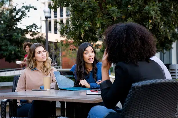 Drei Frauen sitzen an einem Tisch und schauen auf einen Tablet-Computer