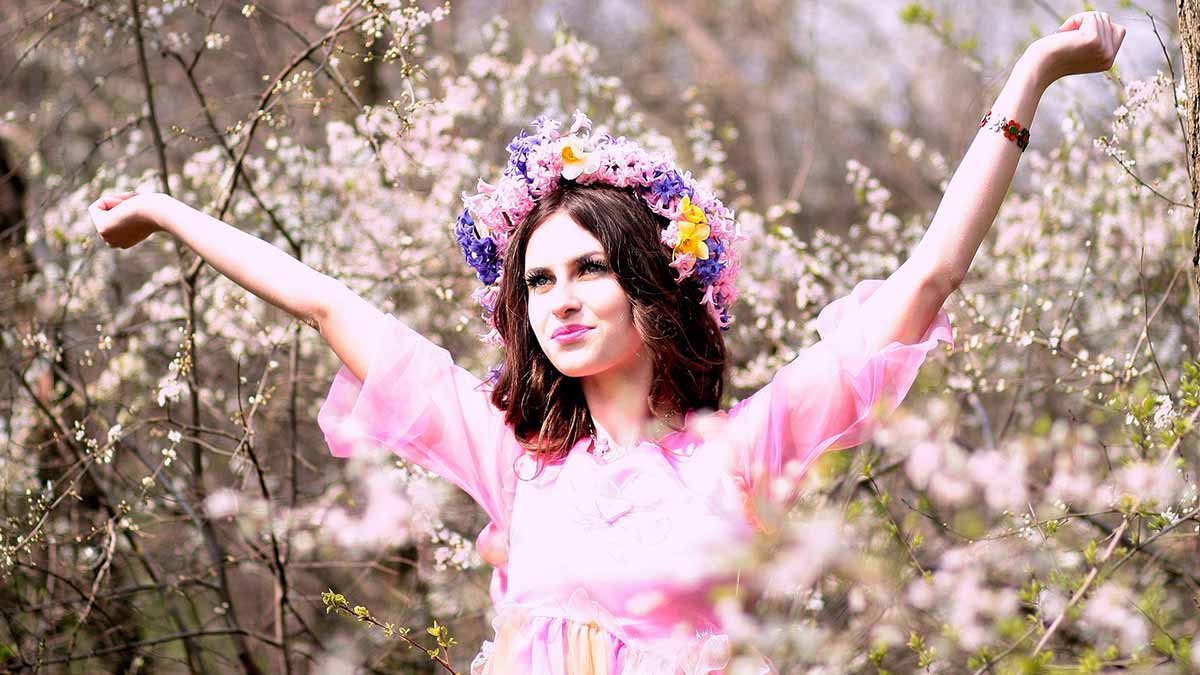 Fröhliche Frau, die ein rosa Kleid und eine Blumenkrone in einem Feld mit rosa Blumen trägt.