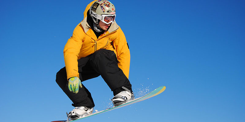 Pessoa vestindo uma jaqueta amarela e calças de neve pretas snowboard