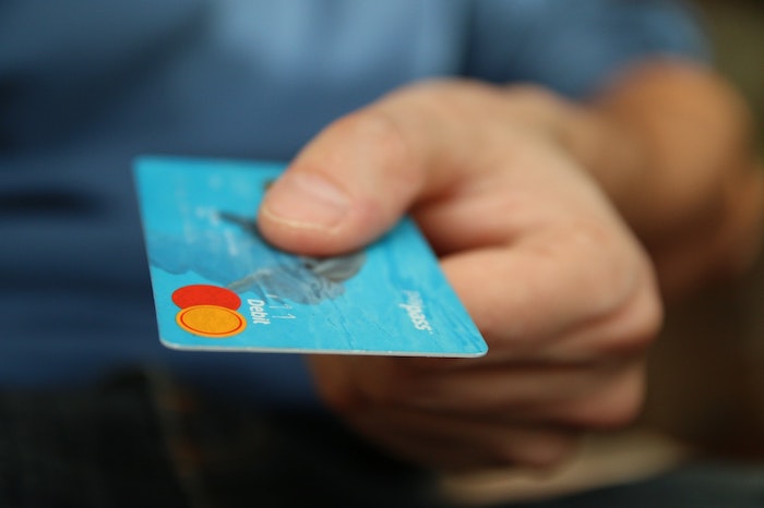 Persoană care întinde o mână ținând un card de debit