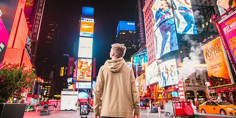 Mężczyzna stojący na TimeSquare i wpatrujący się w cyfrowe ekrany