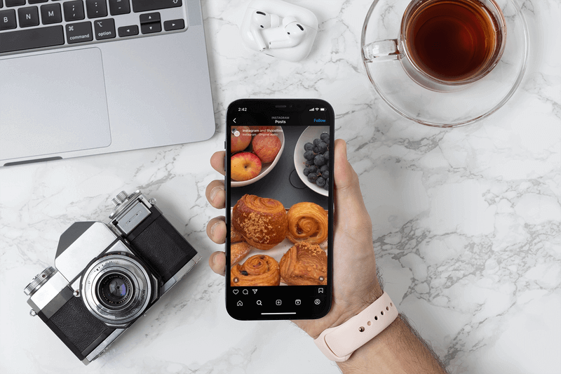 Mockup di un fotografo che tiene un Iphone 12 Pro Max sopra la sua scrivania