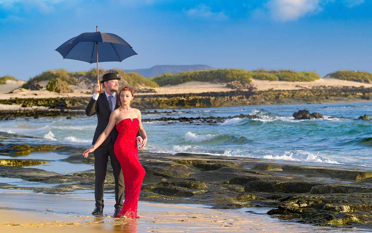 Mann im blauen Anzug mit Frau im roten Kleid am Strand.