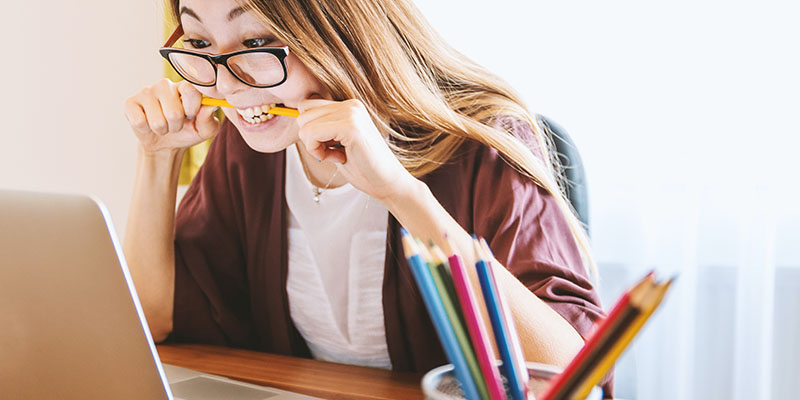 Eine Frau kaut nervös auf einem Bleistift, während sie an ihrem Laptop arbeitet.