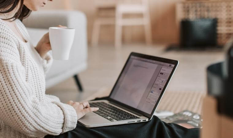 femme écrivant sur un ordinateur et buvant du café