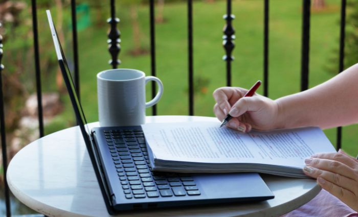 personne assise à une table avec un ordinateur en train de relire un document