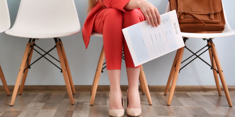 mujer esperando en una silla con un currículum en la mano