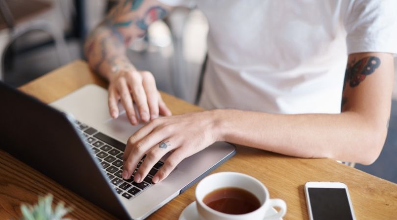 Mann mit Tätowierungen, der am Computer tippt