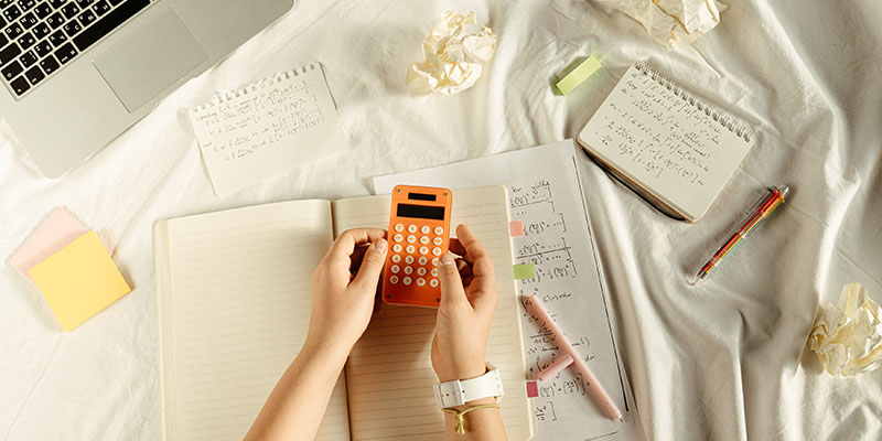 Person hält einen orange-weißen Taschenrechner über einem Mathematikbuch