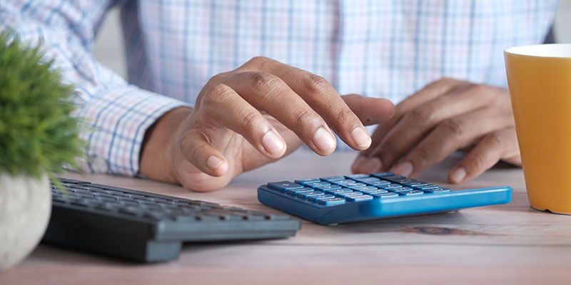 Um homem usando duas calculadoras em uma mesa marrom