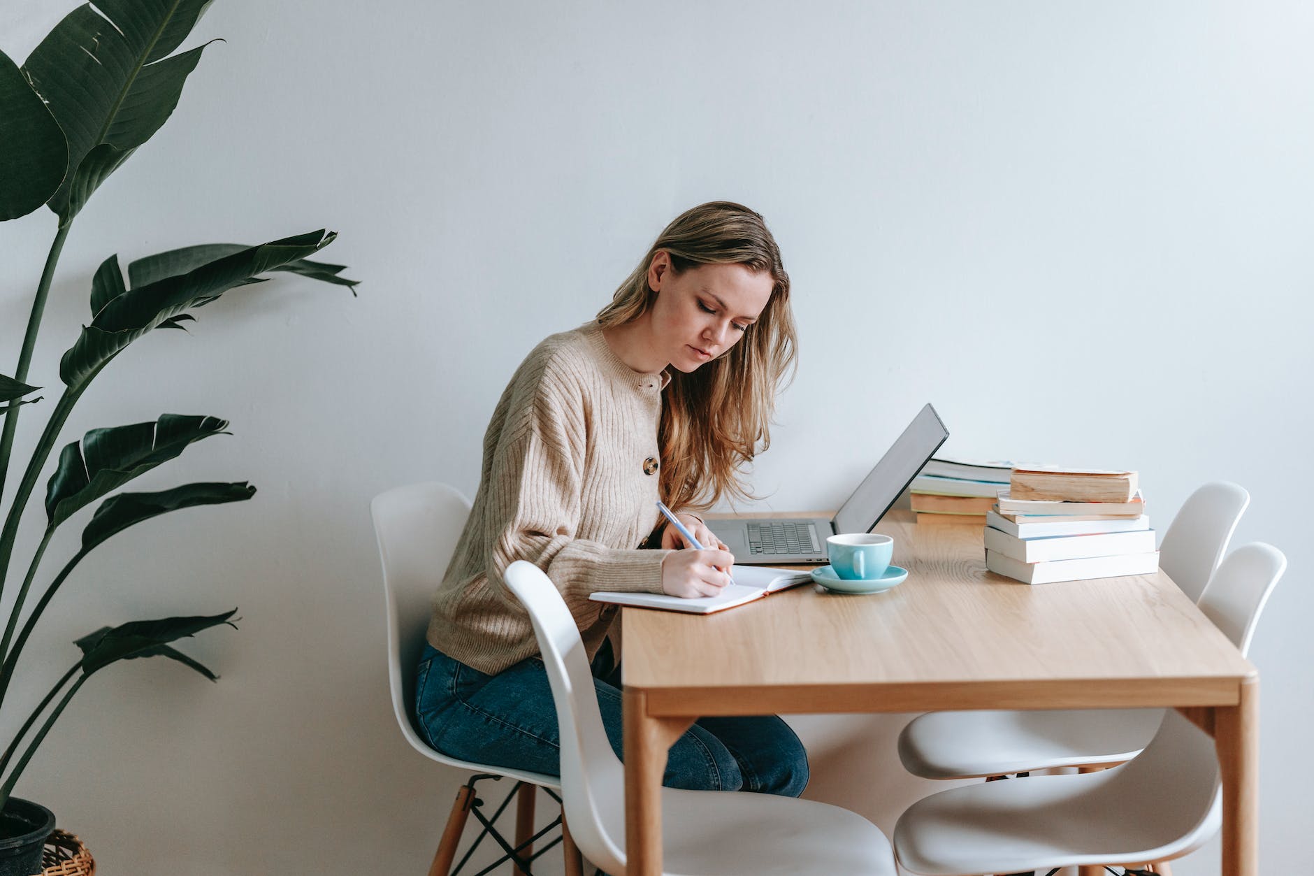 focused woman writing in notebook at table with laptop