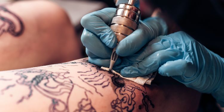 tatuator care lucrează la tatuajul cuiva