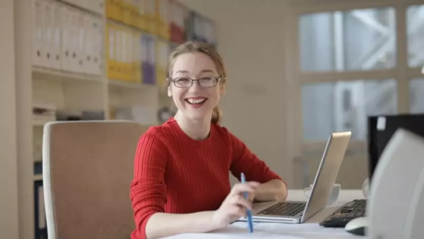 Eine lächelnde Frau sitzt mit einem Laptop an einem Schreibtisch und lernt Content-Marketing-Strategien.