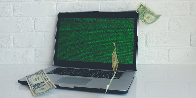 جهاز كمبيوتر محمول أسود رمادي مع شاشة خضراء وفواتير الدولار تتطاير حوله