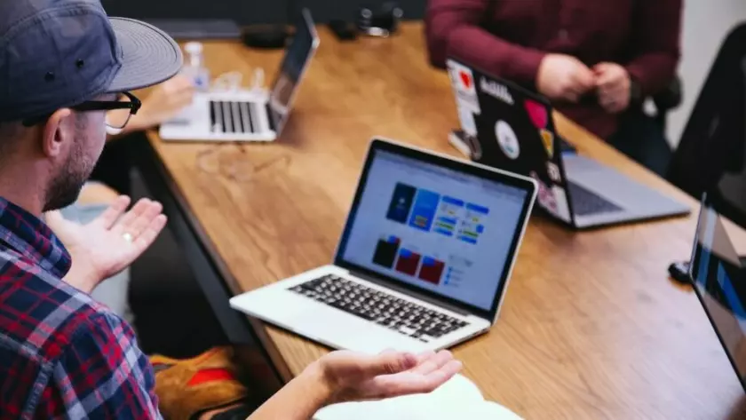 Um grupo de pessoas sentadas ao redor de uma mesa com laptops.