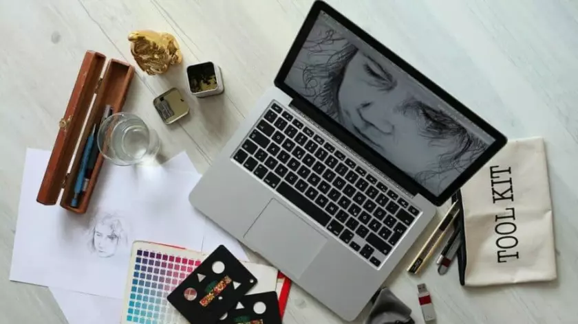 Um laptop em uma mesa ao lado de materiais de arte está pronto para encontrar algumas dicas de crescimento de negócios para artistas.