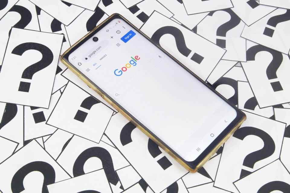 هاتف محمول على صفحة Google الرئيسية محاط بعلامات الاستفهام