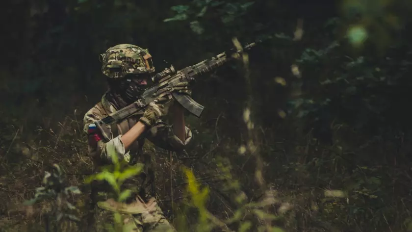 Żołnierz w kamuflażu trzyma karabin w lesie.