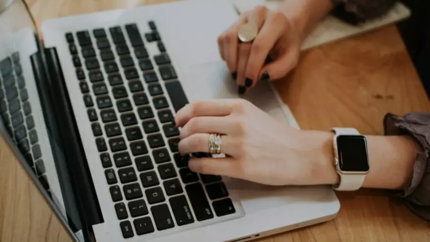 Una mujer escribiendo en una computadora portátil con un Apple Watch.