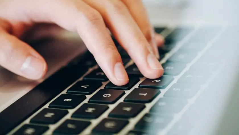 La mano de una persona está escribiendo en el teclado de una computadora portátil.