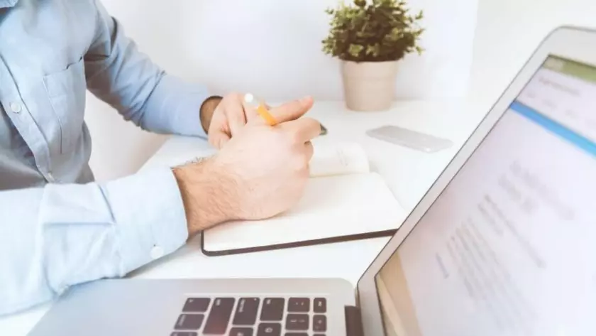 Un hombre sentado en un escritorio con una computadora portátil, una libreta y un bolígrafo.