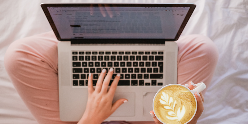 Uma mulher digitando em seu laptop enquanto toma café