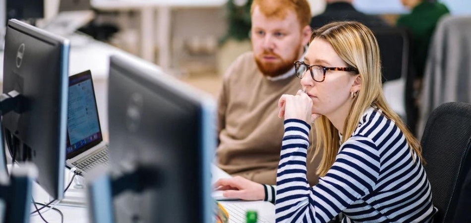 Ein weiblicher und ein männlicher Gripped-Mitarbeiter saßen beide an einem Schreibtisch und blickten auf denselben Computerbildschirm.